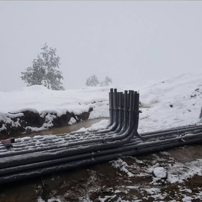 Black electrical conduits rising out of a snowy hillside trench