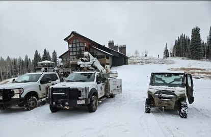 Two Current Electric service trucks parked in snow at a mountain resort lodge