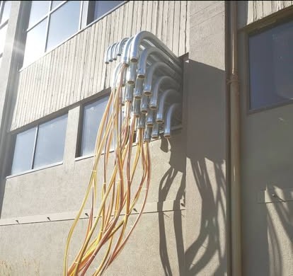 Rigid conduit bends on a building exterior with wire being pulled through