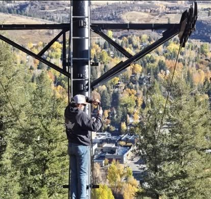 A worker on a tall steel tower high above an autumn mountain valley