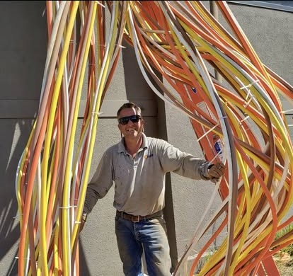 An electrician with large bundles of colored conduit against a building wall