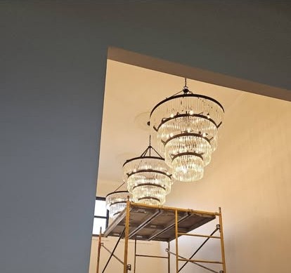 A crystal chandelier being installed from yellow scaffolding in a vaulted room